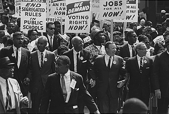 Leaders of the 1963 March on Washington walking down the street arm in arm.